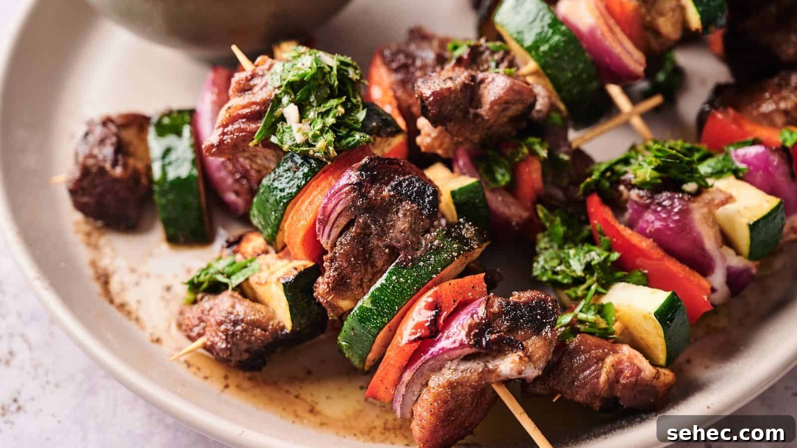 17 Budget Cookout Recipes That Save Room for Better Burgers 2 Grilled meat and vegetable skewers with zucchini, red onion, and red bell pepper, garnished with chopped herbs, served on a beige plate.