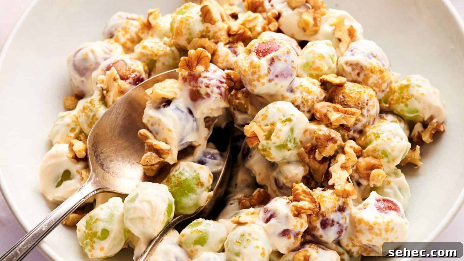 17 Budget Cookout Recipes That Save Room for Better Burgers 14 A bowl of grape salad with green and red grapes coated in creamy dressing, topped with chopped walnuts and brown sugar, with a spoon for serving.