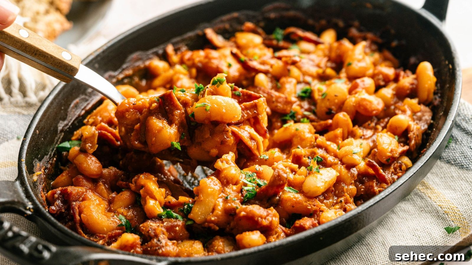 17 Budget Cookout Recipes That Save Room for Better Burgers 17 A black oval dish filled with baked beans in a rich sauce, mixed with pieces of bacon and garnished with chopped parsley.