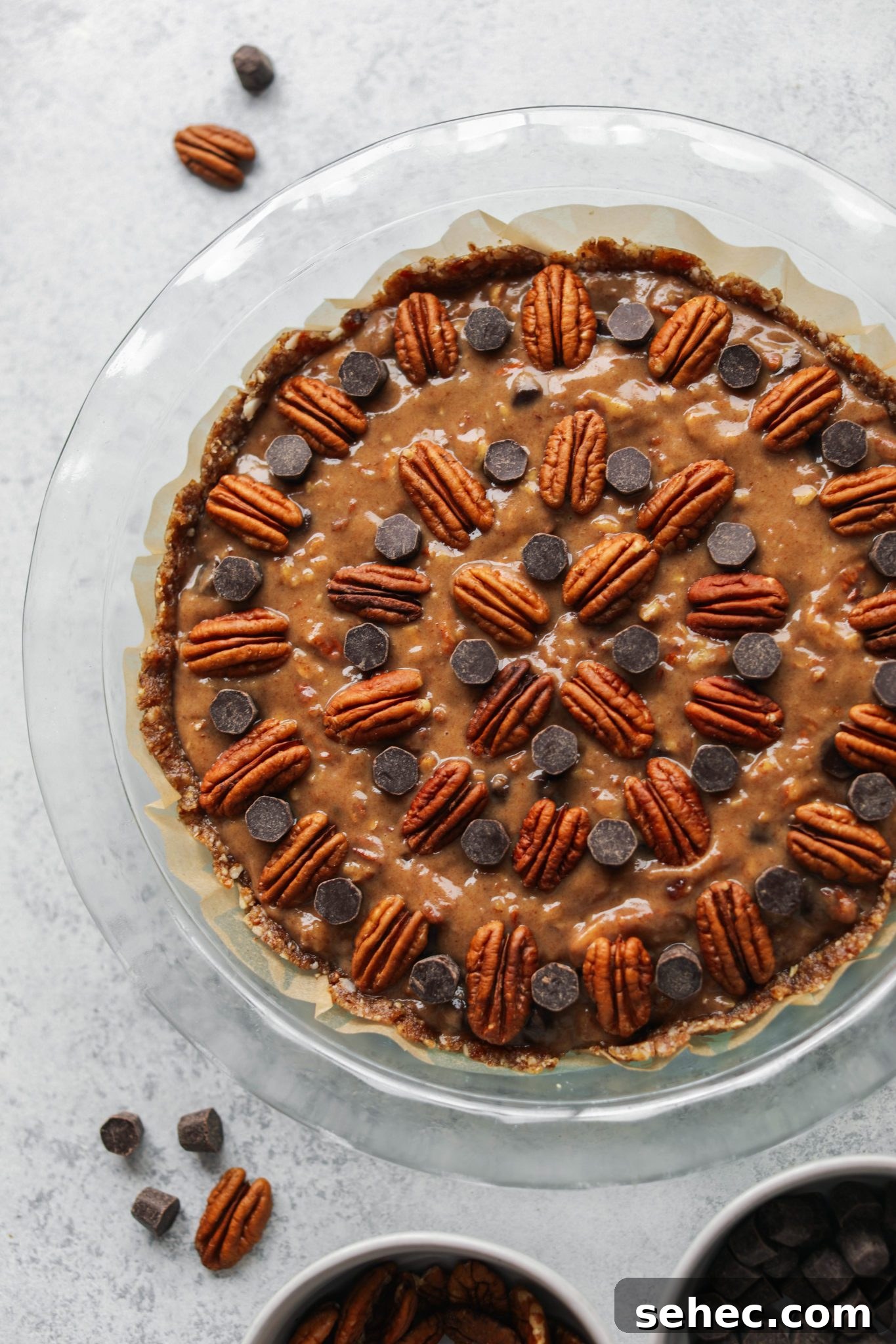 Vegan Dark Chocolate Pecan Pie Recipe 6 Pecan Pie filling topped with dark chocolate chips and pecans in pie pan by Flora & vino