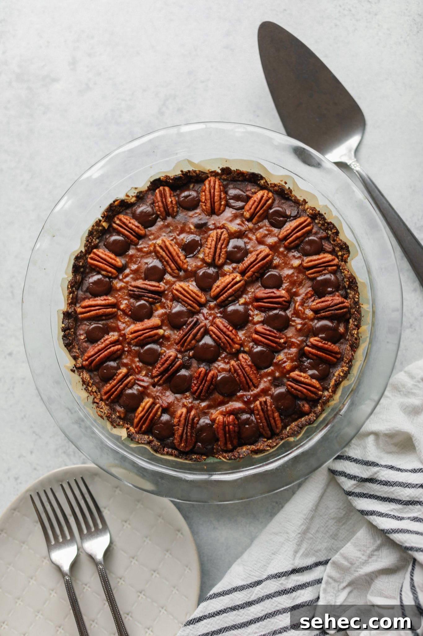 Vegan Dark Chocolate Pecan Pie Recipe 7 Vegan Dark Chocolate Pecan Pie baked in pie pie with pie server and plates and forks by Flora & vino