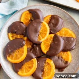Chocolate Dipped Candied Orange Slices with Gift Tags 11 A mottled blue platter of candied orange slices dipped in chocolate with oranges and kitchen equipment around them.