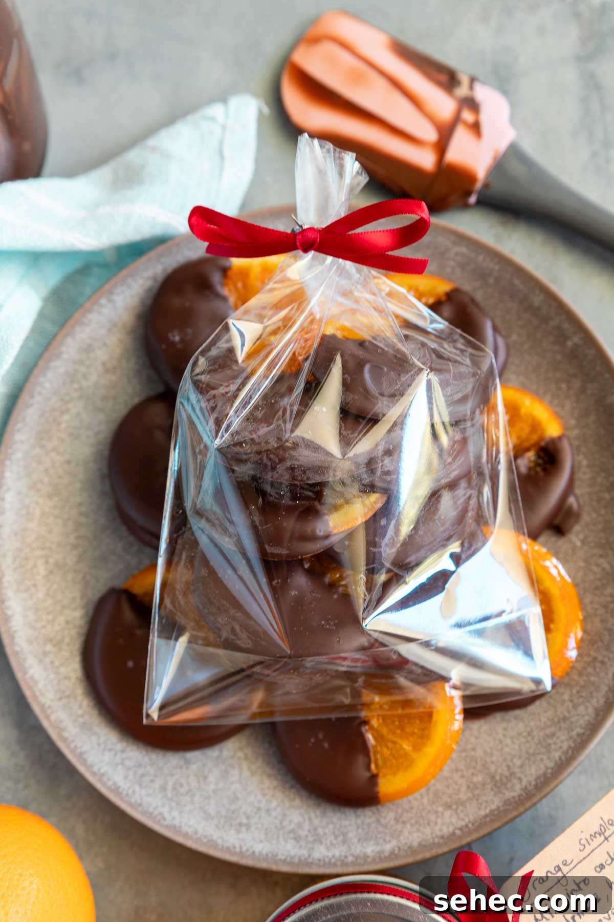Chocolate Dipped Candied Orange Slices with Gift Tags 9 A small clear gift bag filled with candied oranges dipped in chocolate, placed on a blue plate with more orange slices.