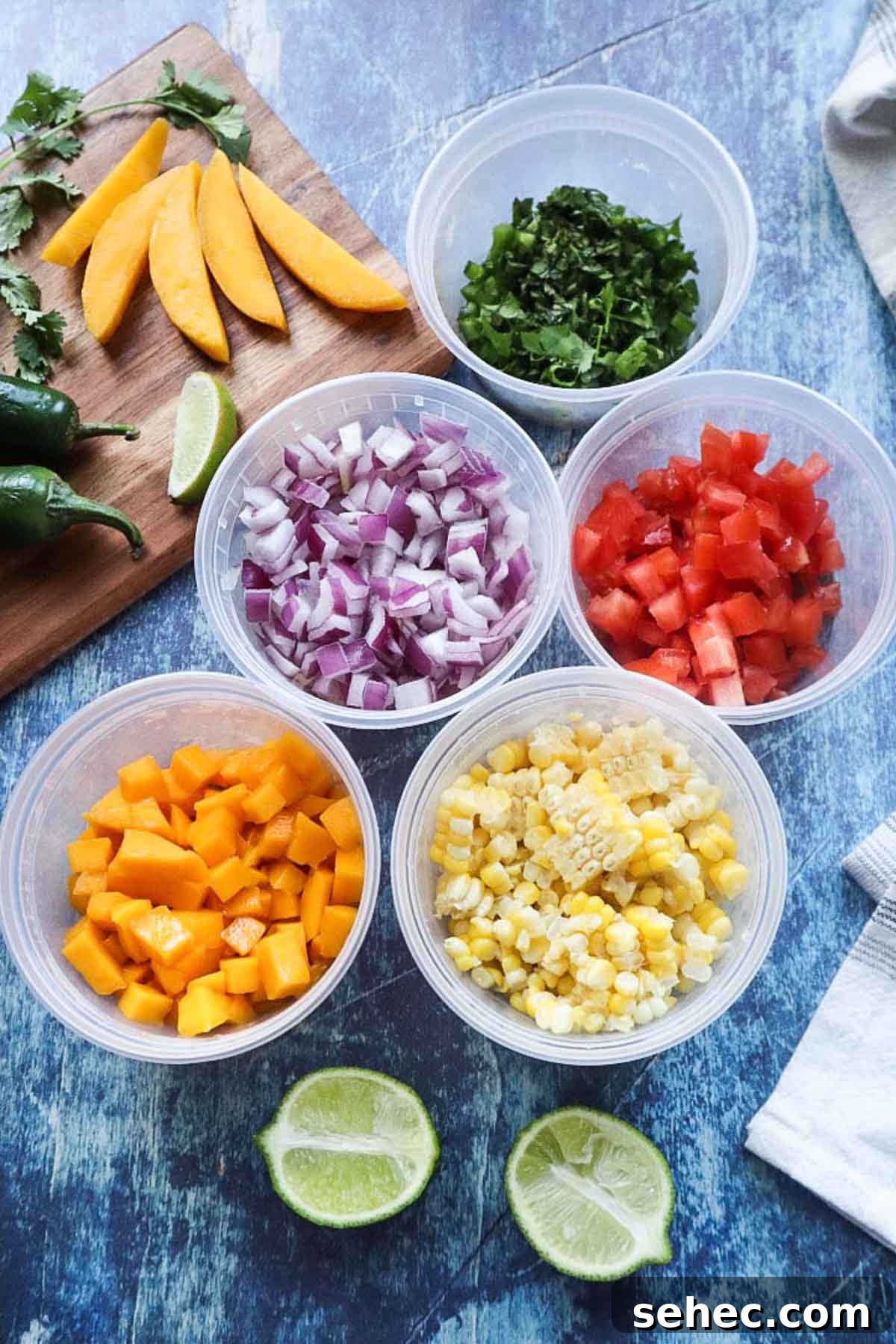 plastic tupperware containers that contain chopped cilantro, red onion, tomato, mango, and corn, with lime.