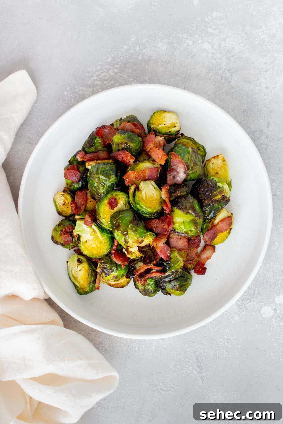 Crispy Air Fryer Brussels Sprouts with Bacon 8 Overhead view of a white plate with air fryer brussels sprouts and bacon with a linen on the side.
