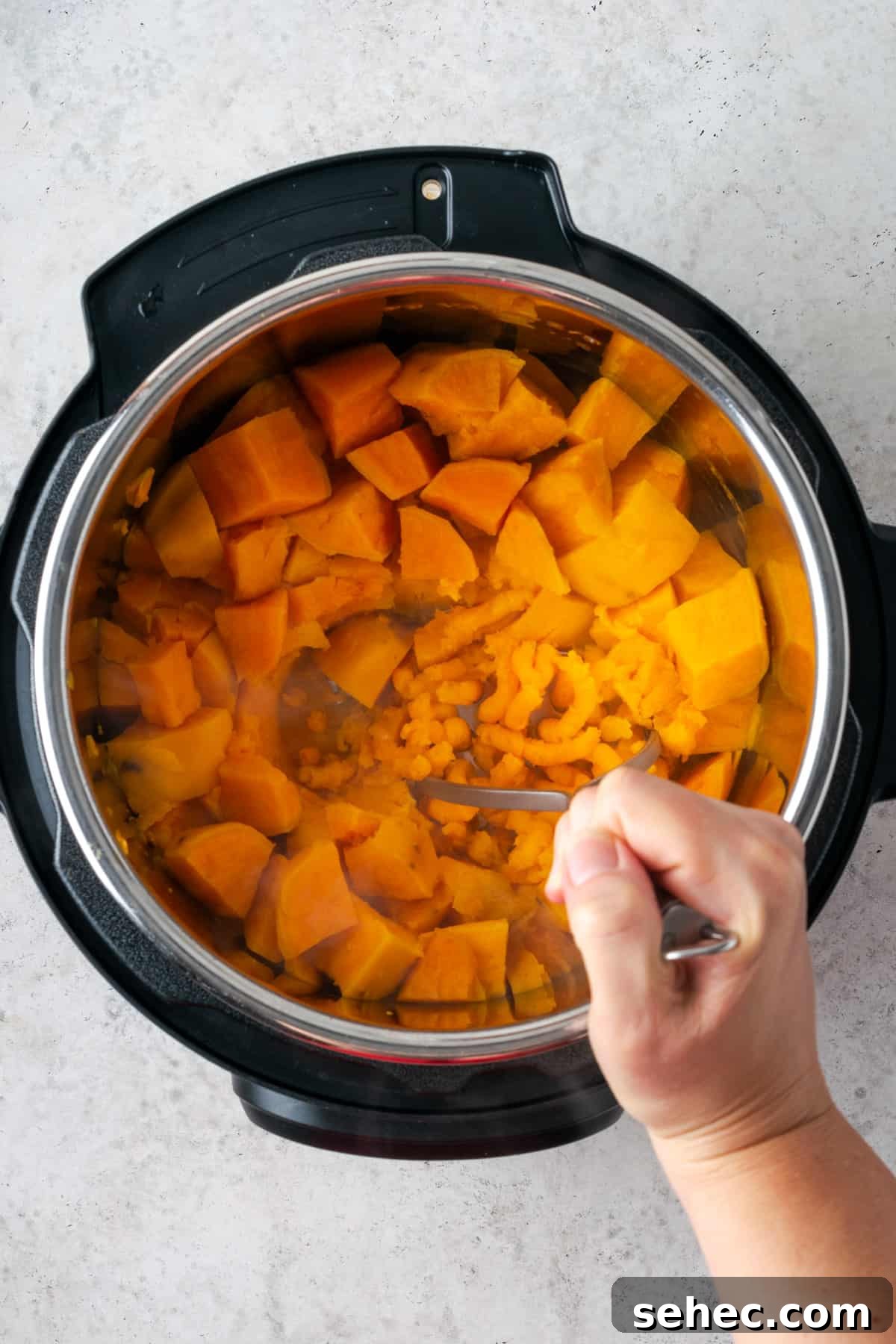 Creamy Instant Pot Mashed Sweet Potatoes 5 A potato masher being used to smash cooked sweet potatoes.