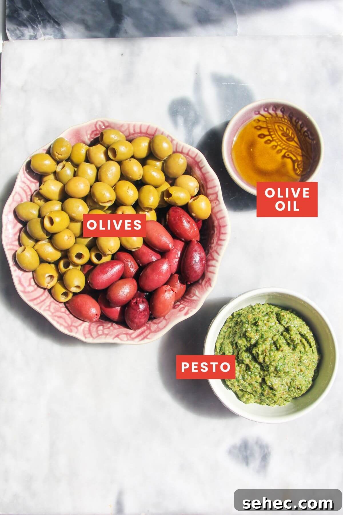 Pesto Marinated Olives Recipe 3 Ingredients for pesto marinated olives laid out on a grey marble background and labelled.