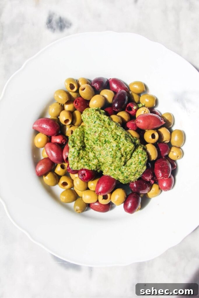 Pesto Marinated Olives Recipe 4 Basil pesto on top of olives in a white bowl.