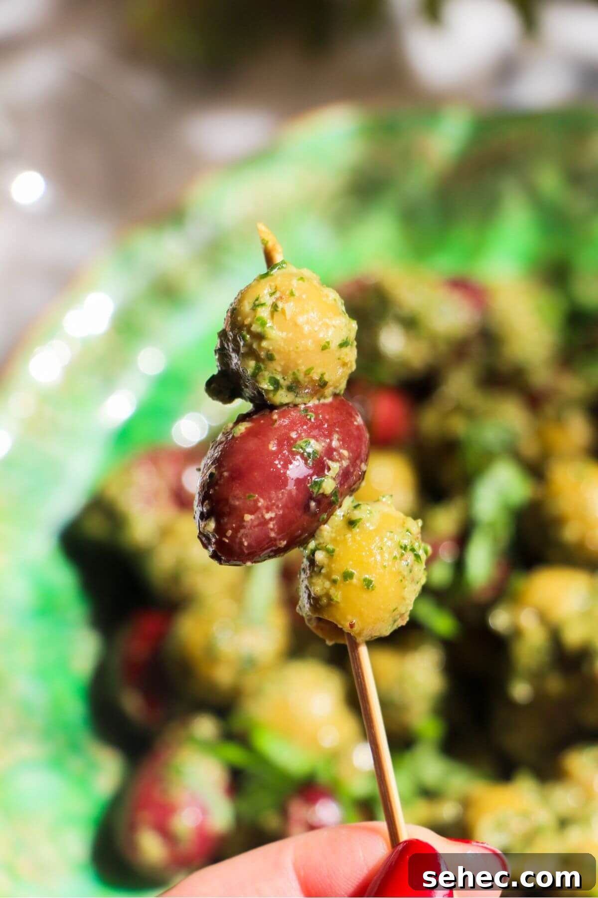 Pesto Marinated Olives Recipe 6 Three pesto marinated olives on a small skewer with more olives in the background.