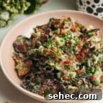 Smashed potato salad in a pink bowl with chives scattered on top.