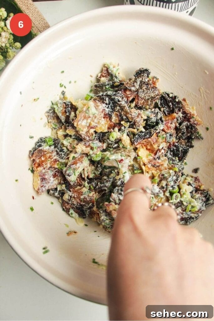 Crispy Smashed Potato Salad with Tzatziki Sauce 10 Hand holding spoon mixing smashed potato salad in a bowl.