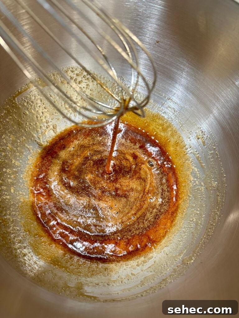 Brown Butter Buttercream Frosting Recipe 5 A whisk stirring brown sugar and egg whites in a bowl.