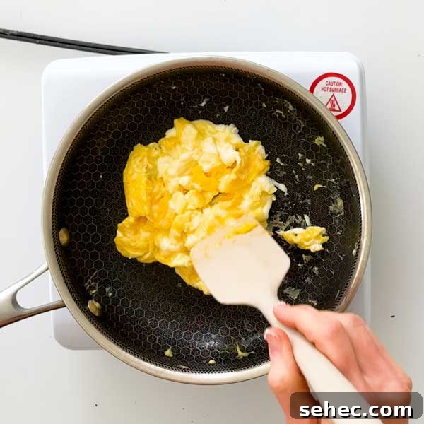 High Protein Loaded Baked Sweet Potato Breakfast 12 Scrambling eggs in a skillet with a spatula.