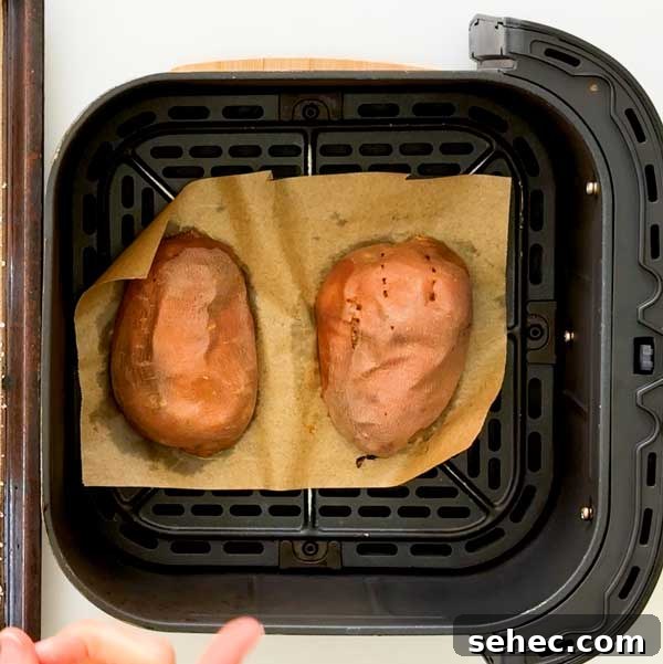 High Protein Loaded Baked Sweet Potato Breakfast 7 Two sweet potato halves flesh side down on parchment paper in an air fryer basket.