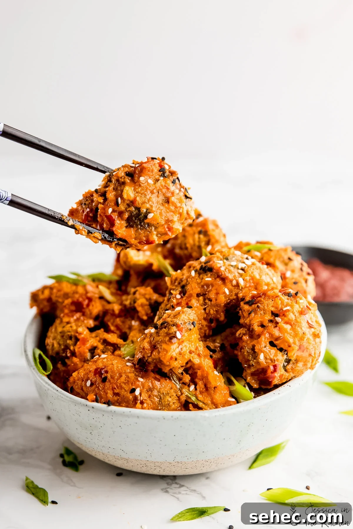 Vegan Bang Bang Broccoli with Creamy Spicy Sauce 2 Bang bang broccoli being held by chopsticks over a bowl with more bang bang broccoli in it.