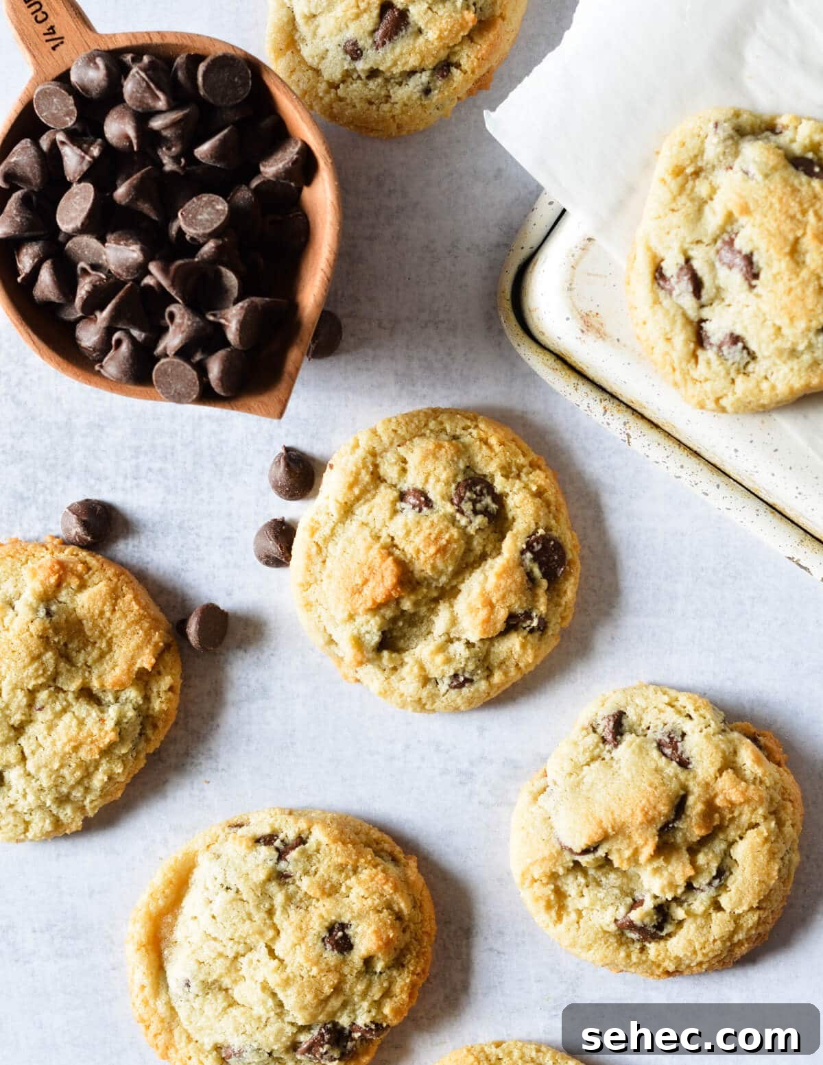 Chewy Almond Flour Chocolate Chip Cookies 2 almond flour chocolate chip cookies near a cup of chocolate chips.