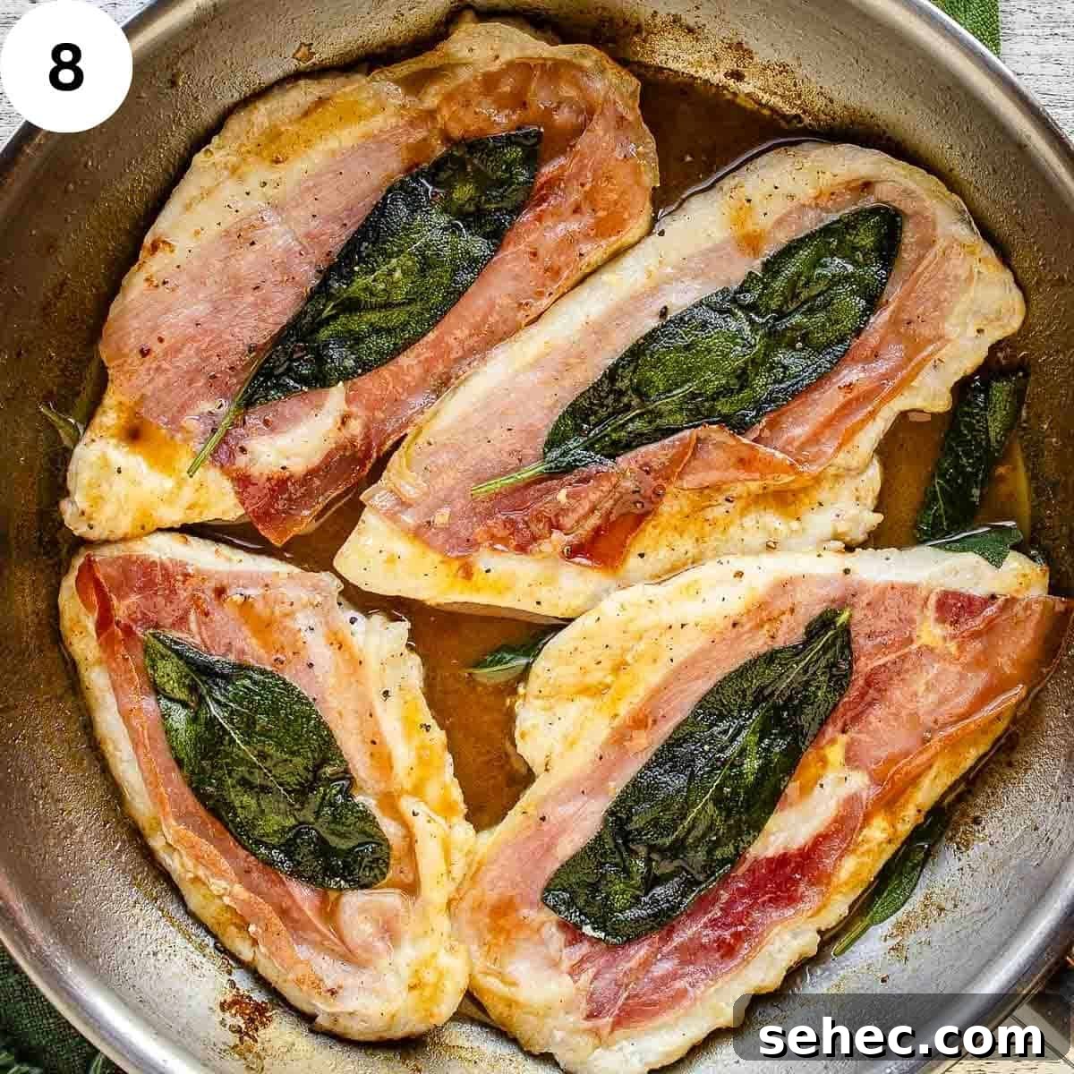 Chicken Saltimbocca with Prosciutto and Sage 11 Four cooked chicken breasts each with prosciutto and a sage leaf in a pan.