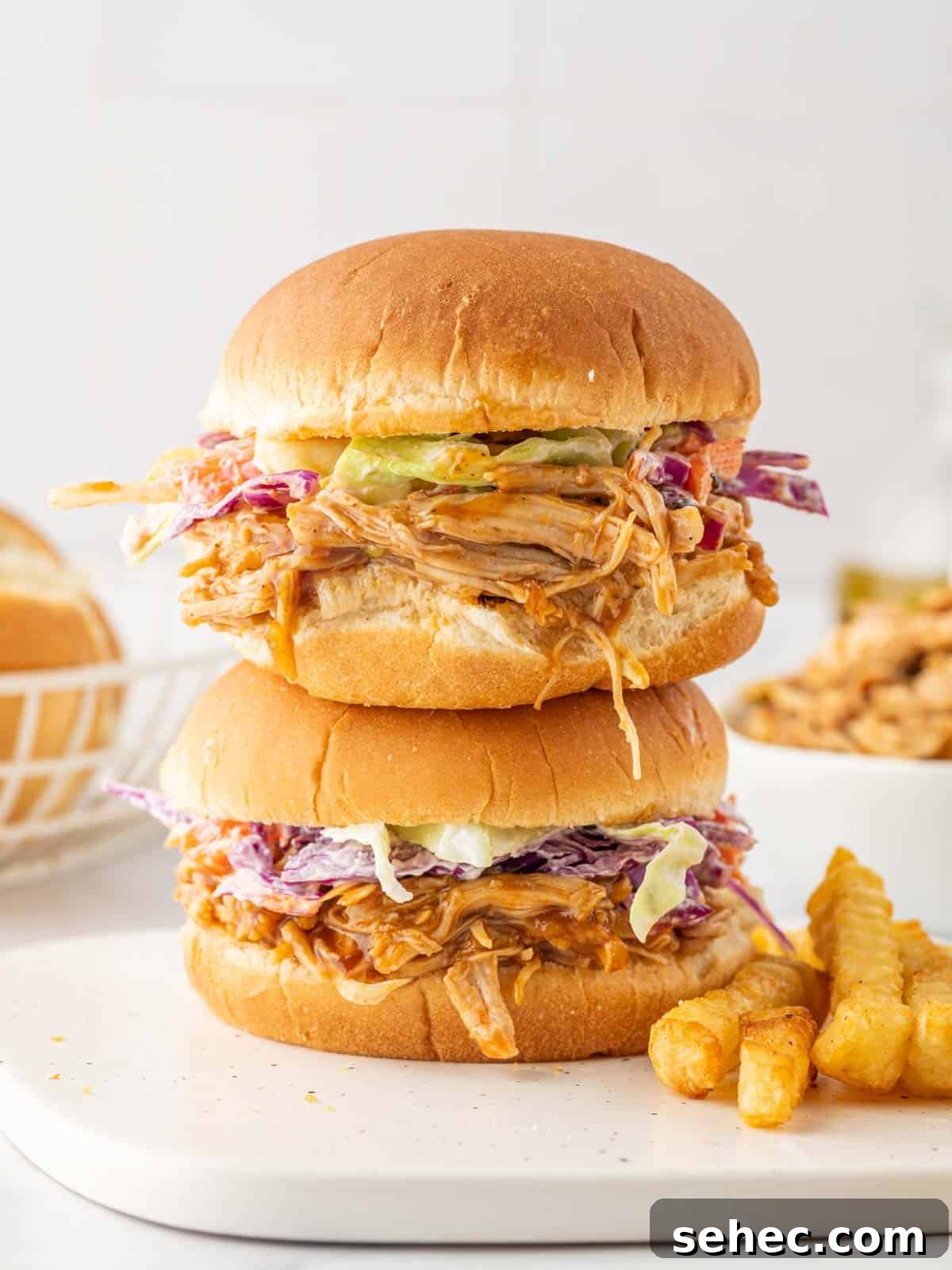 BBQ Pulled Chicken Burger with Smoky Sauce 9 Two chicken burgers are stacked on a plate with fries.