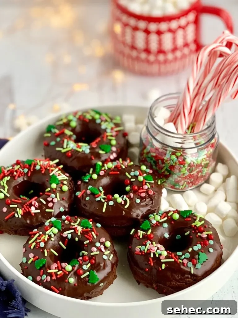 Double Chocolate Donuts with Rich Chocolate Glaze 6 5 double chocolate donuts on a platter with chocolate ganache frosting topped with festive Christmas sprinkles next to a jar of candy canes.