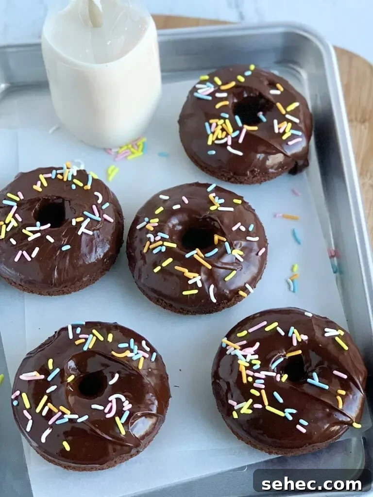 Double Chocolate Donuts with Rich Chocolate Glaze 4 A tray of 5 chocolate donuts after they've been dipped in chocolate ganache frosting and topped with festive Easter colored sprinkles.
