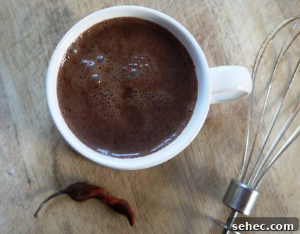 Hot Chilli Chocolate Hot Chilli Chocolate in a white mug beside a chilli and a whisk on a wooden table