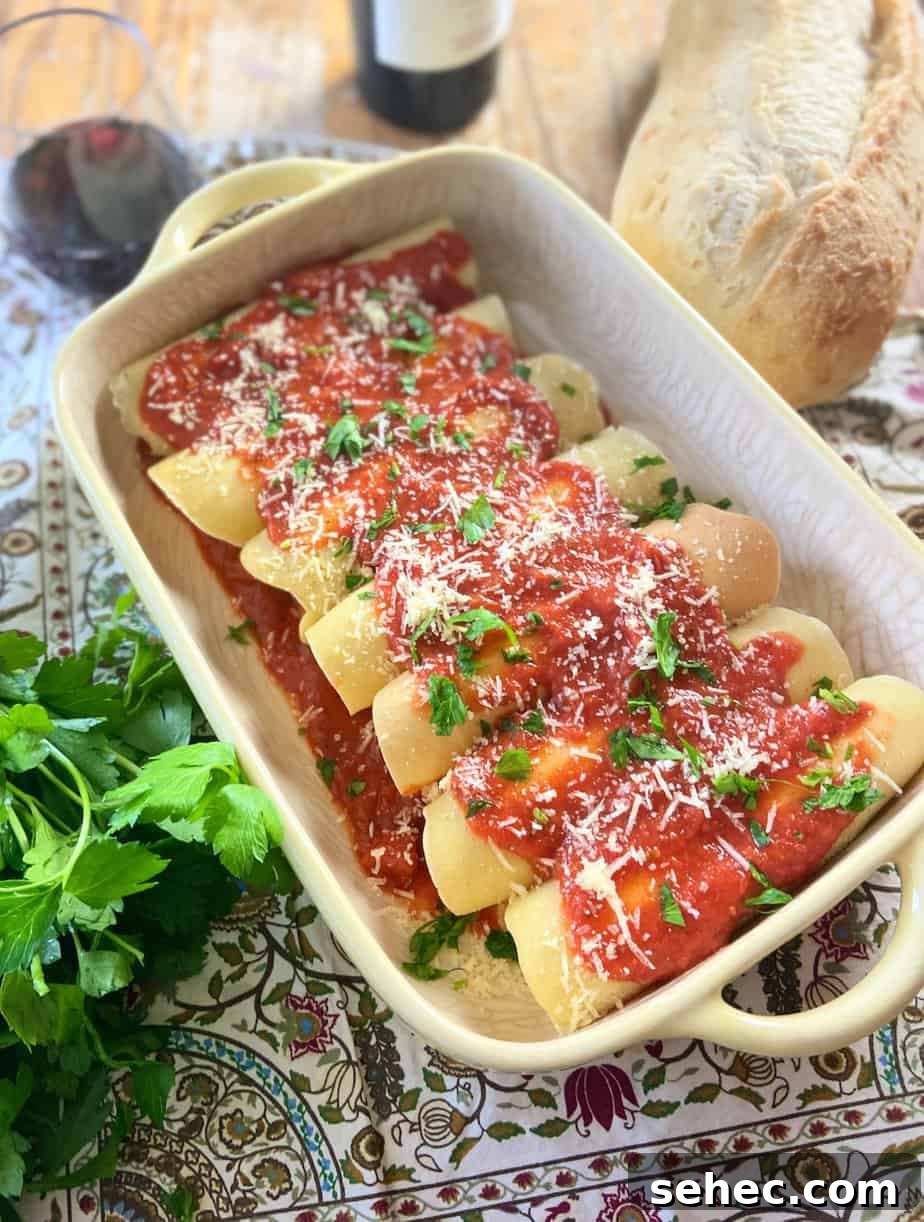 Three Cheese Manicotti Crepes Recipe 2 Manicotti crepes in a yellow baking dish with marinara sauce, grated parmesan cheese and fresh parsley on top.