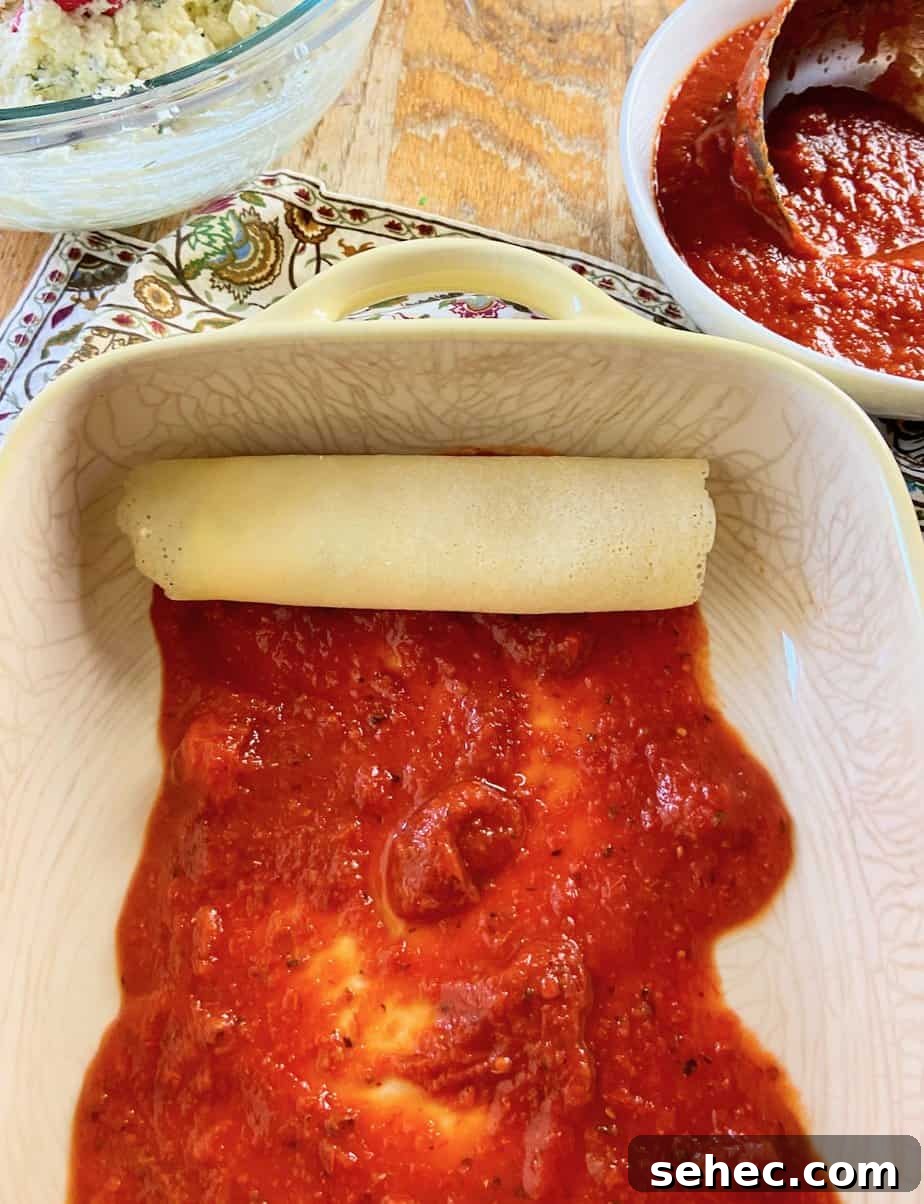 Three Cheese Manicotti Crepes Recipe 8 One rolled manicotti crepe in baking dish with red pasta sauce.