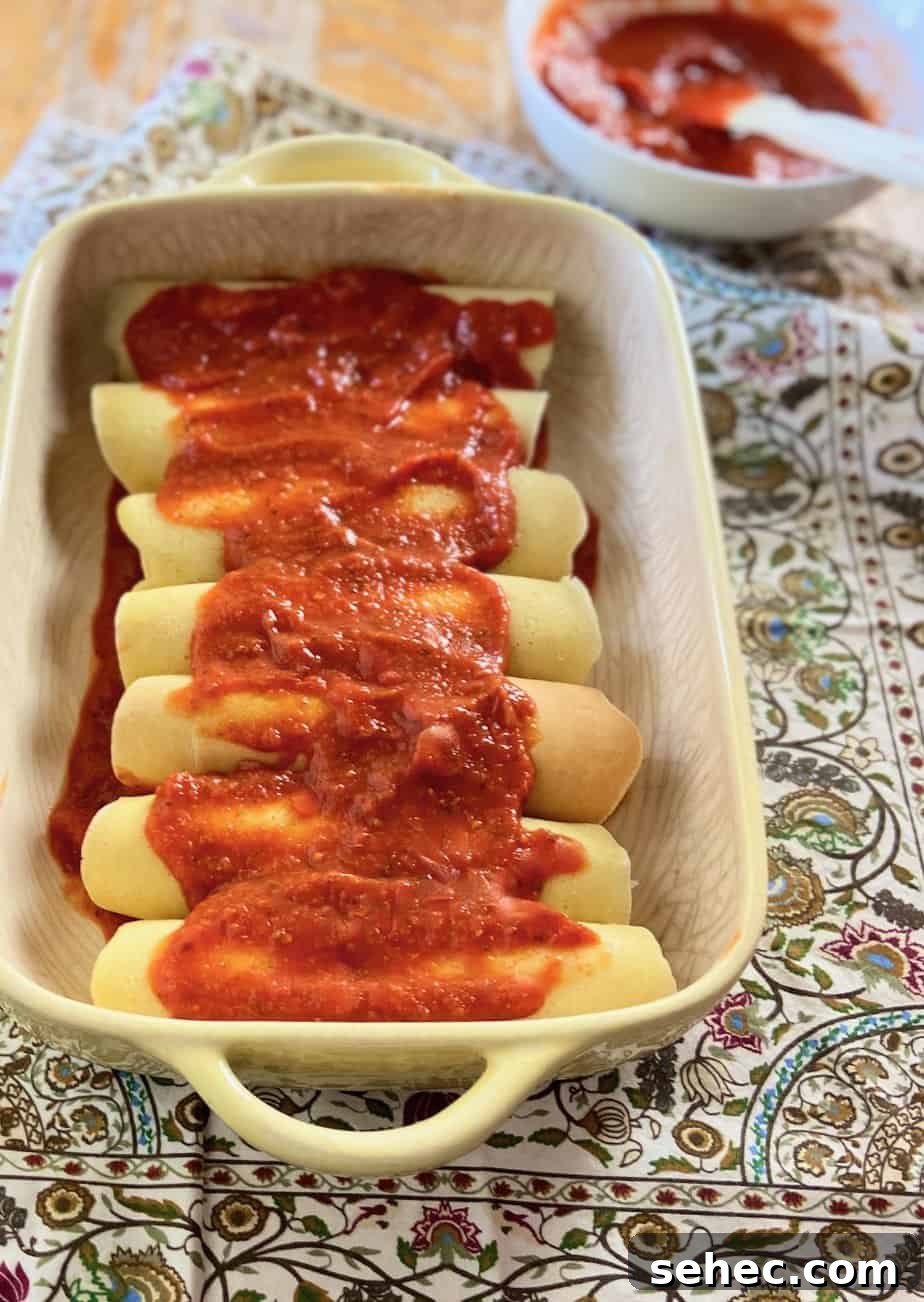 Three Cheese Manicotti Crepes Recipe 9 Manicotti in baking dish topped with red pasta sauce.