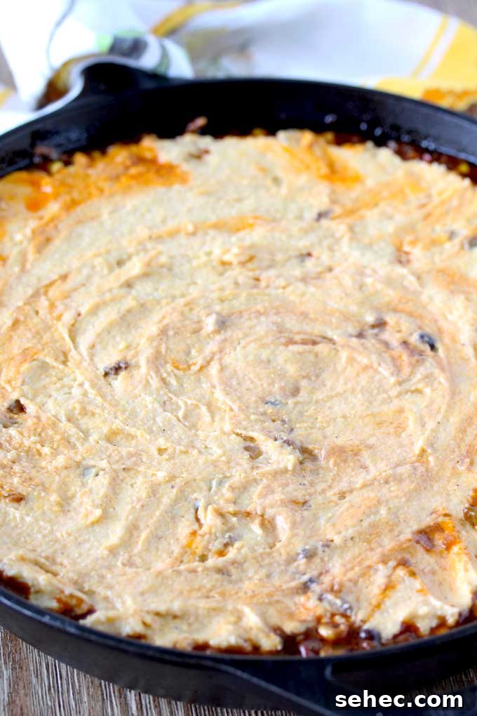 Brown Butter Cornbread Tamale Pie 5 View of a skillet sitting on a wooden surface containing raw cornbread mixture spread over the top of chili.