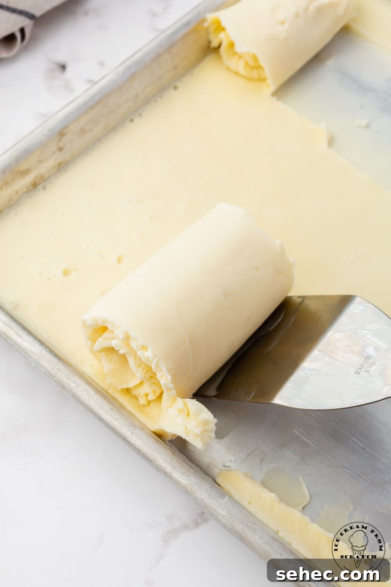 a spatula scraping ice cream rolls off of a sheet pan.