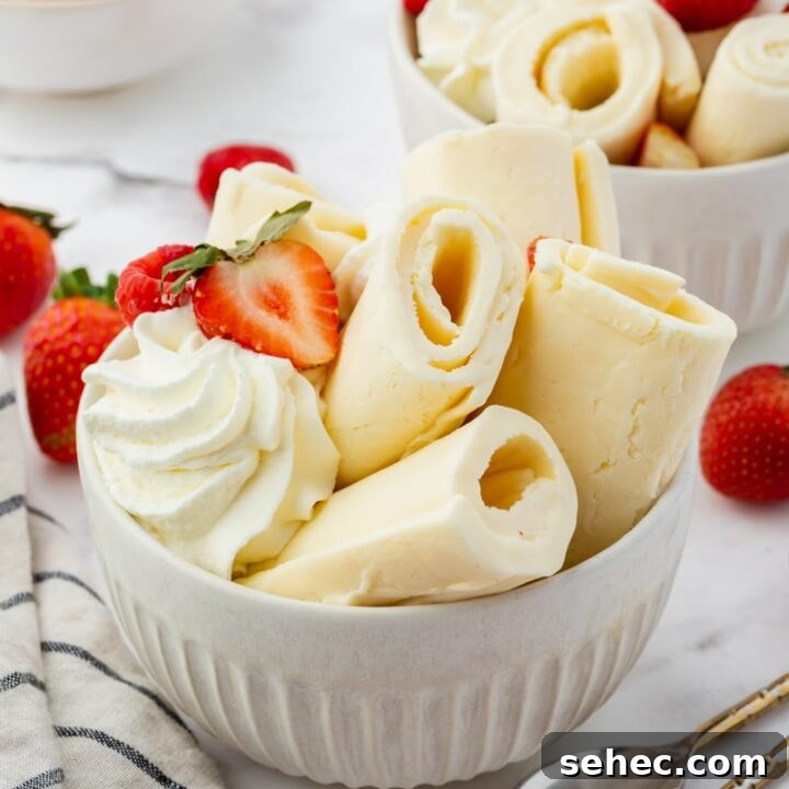 a white bowl filled with rolls of vanilla ice cream, topped with whipped cream and fresh berries. There are two spoons next to the bowl.