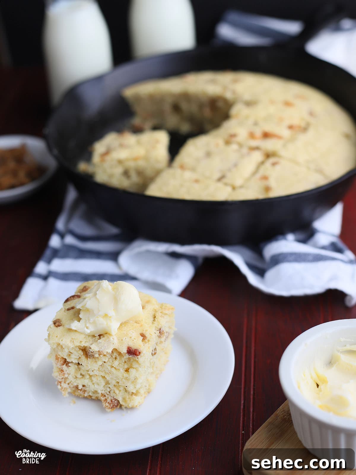 Southern Cracklin Cornbread Recipe 16 side shot of a slice of cracklin' corn bread topped with a dollop of butter on a white plate with a cast iron skillet of bread in the background