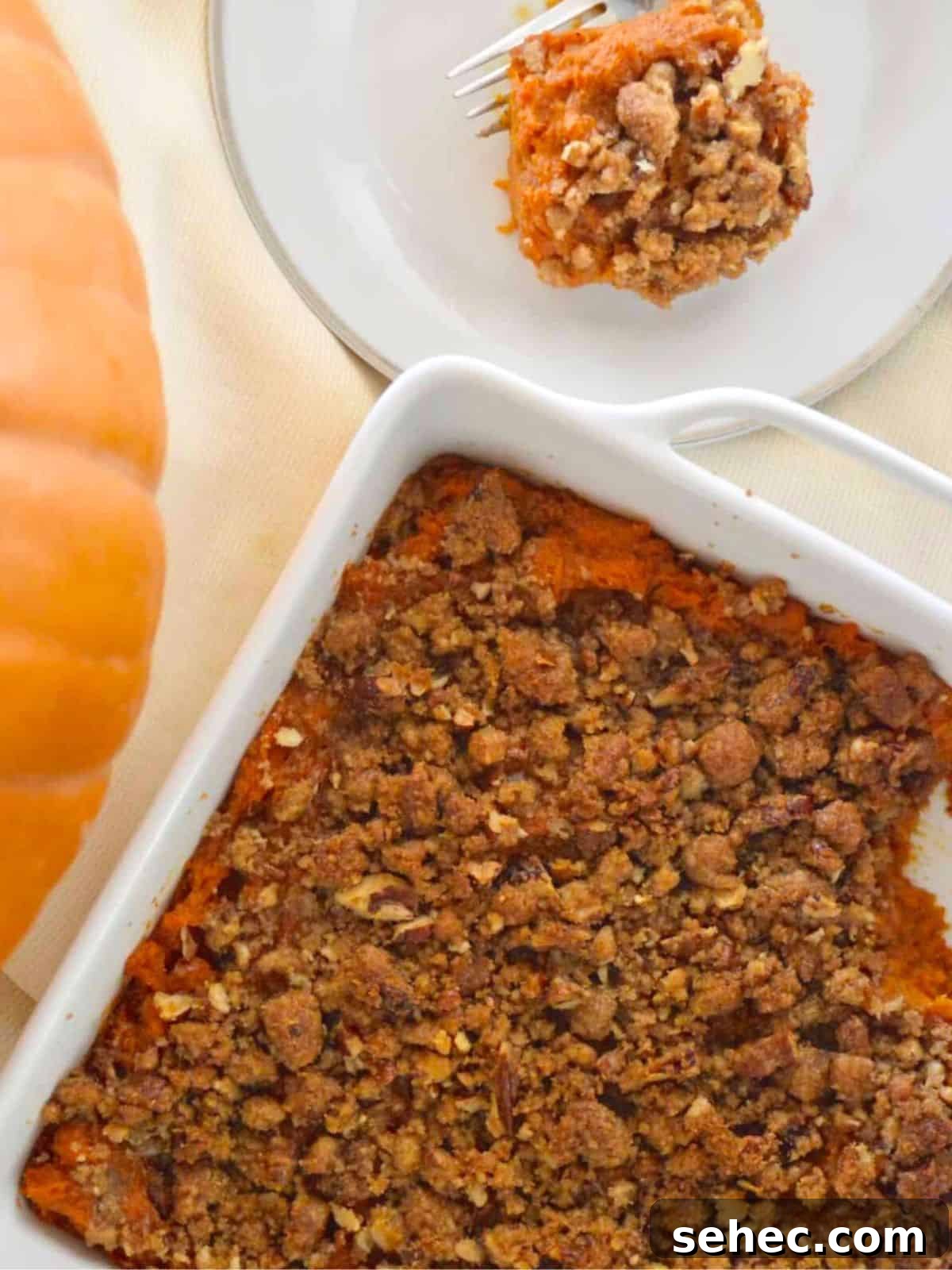 Eggless Sweet Potato Casserole with Pecan Streusel 2 Sweet Potato Casserole with pecan streusel topping on a table with a pumpkin next to it.
