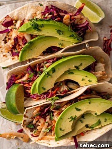 Three tacos topped with slaw and avocado garnished with lime wedges.