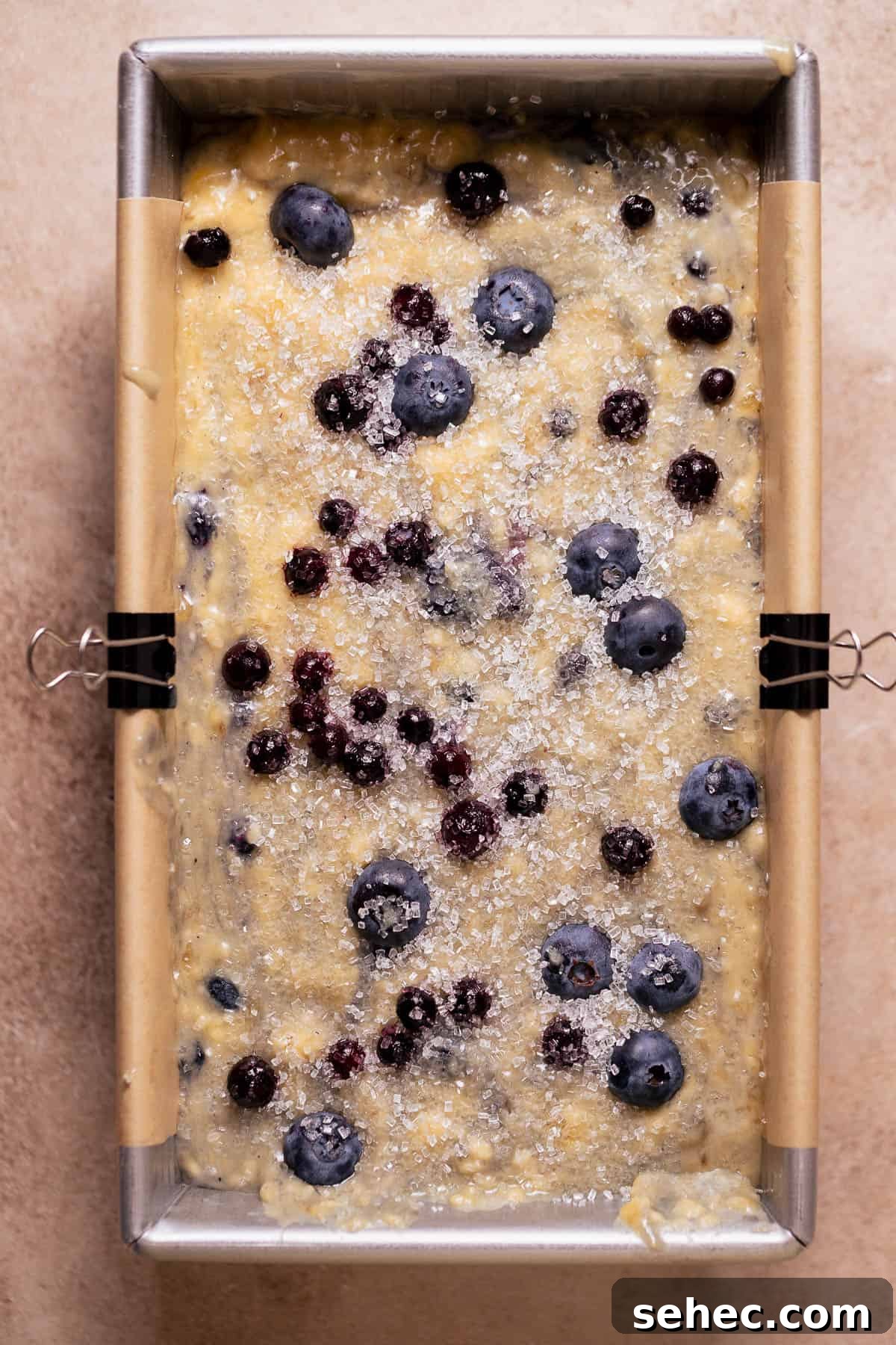 Sugar Crusted Blueberry Banana Bread 5 Unbaked blueberry banana bread batter in a lined loaf pan topped with sugar and berries.