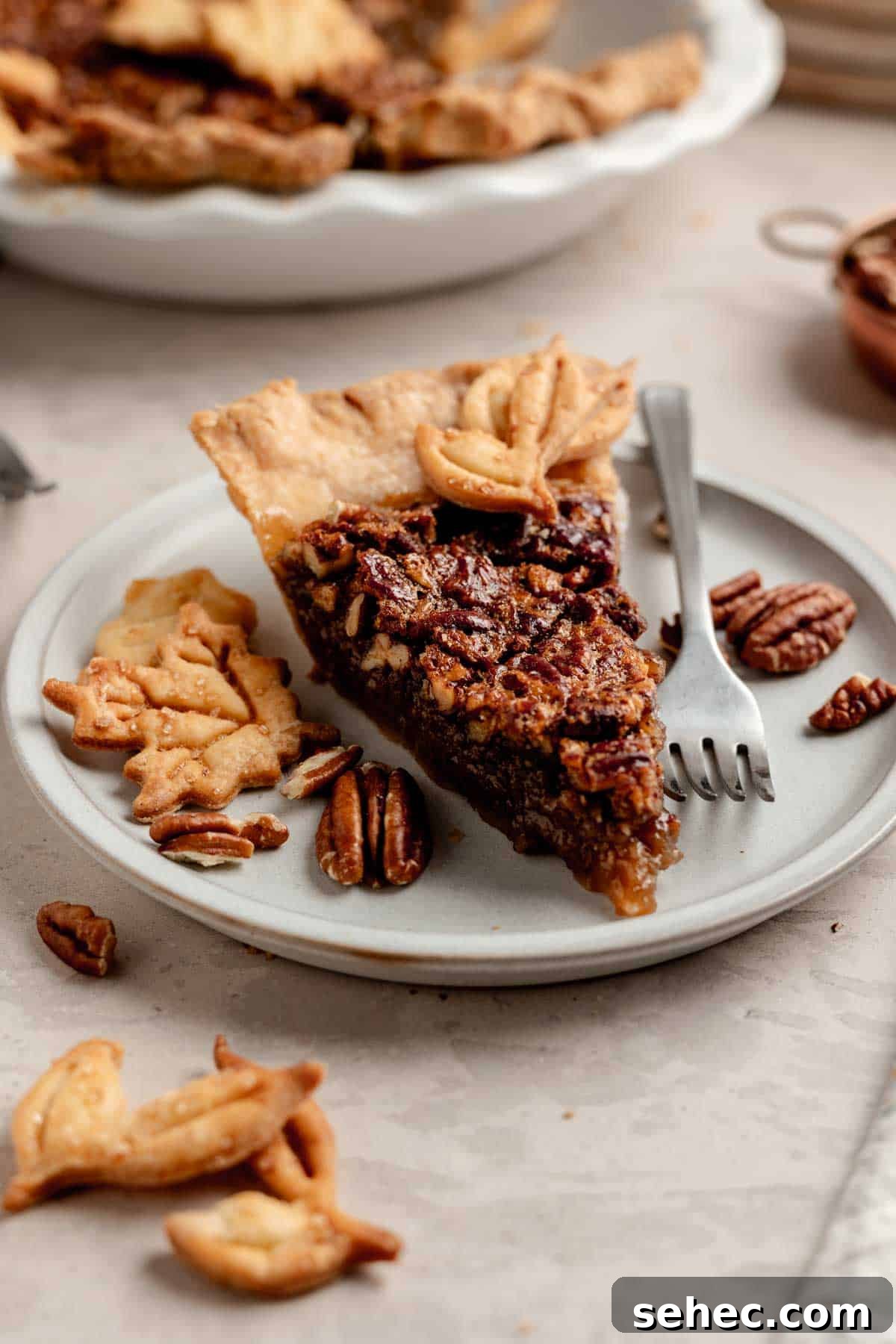 Gluten Free Pecan Pie Recipe with Classic Southern Flavor 8 A slice of gluten-free pecan pie on a small plate next to pecans and leaf-shaped pie crust cut outs.