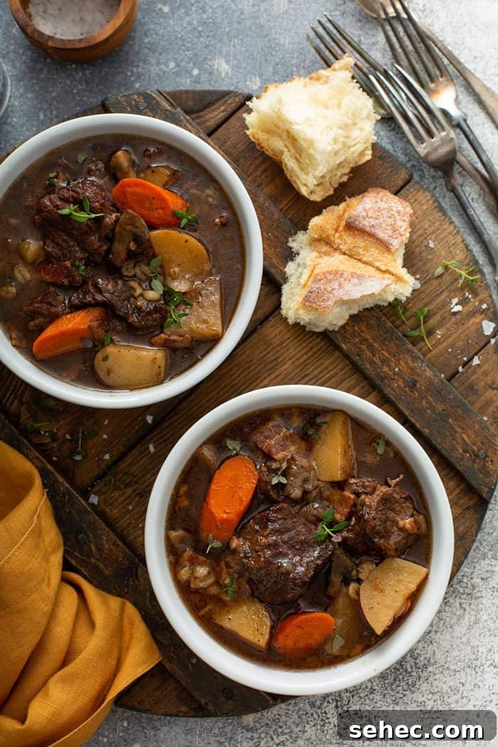 Slow Cooker Beef and Barley Stew Recipe 3 Overhead shot of two white bowls filled with beef and barley stew on a wooden cutting board