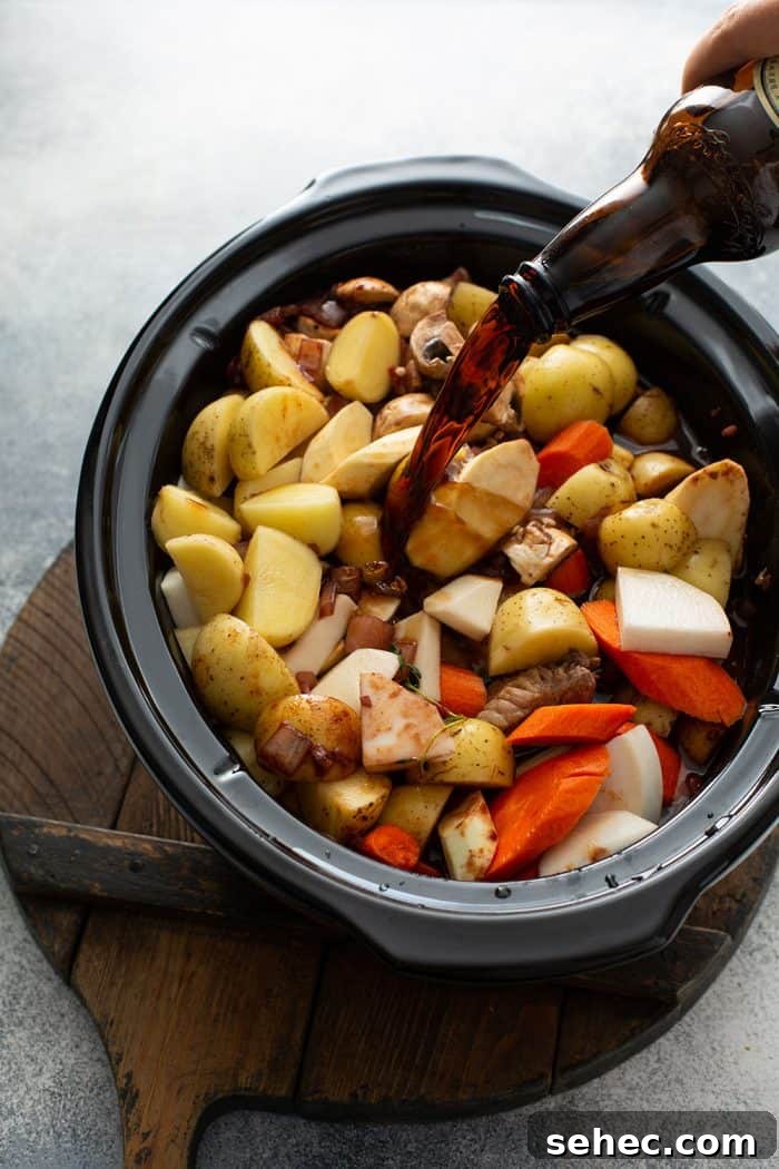 Slow Cooker Beef and Barley Stew Recipe 7 Guinness beer being poured over cut root vegetables in a slow cooker for beef and barley stew