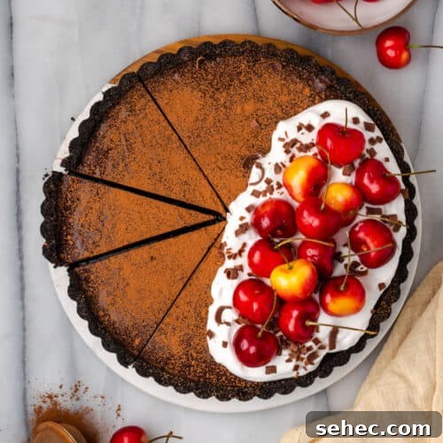 A sliced chocolate ganache tart topped with whipped cream and fresh cherries.