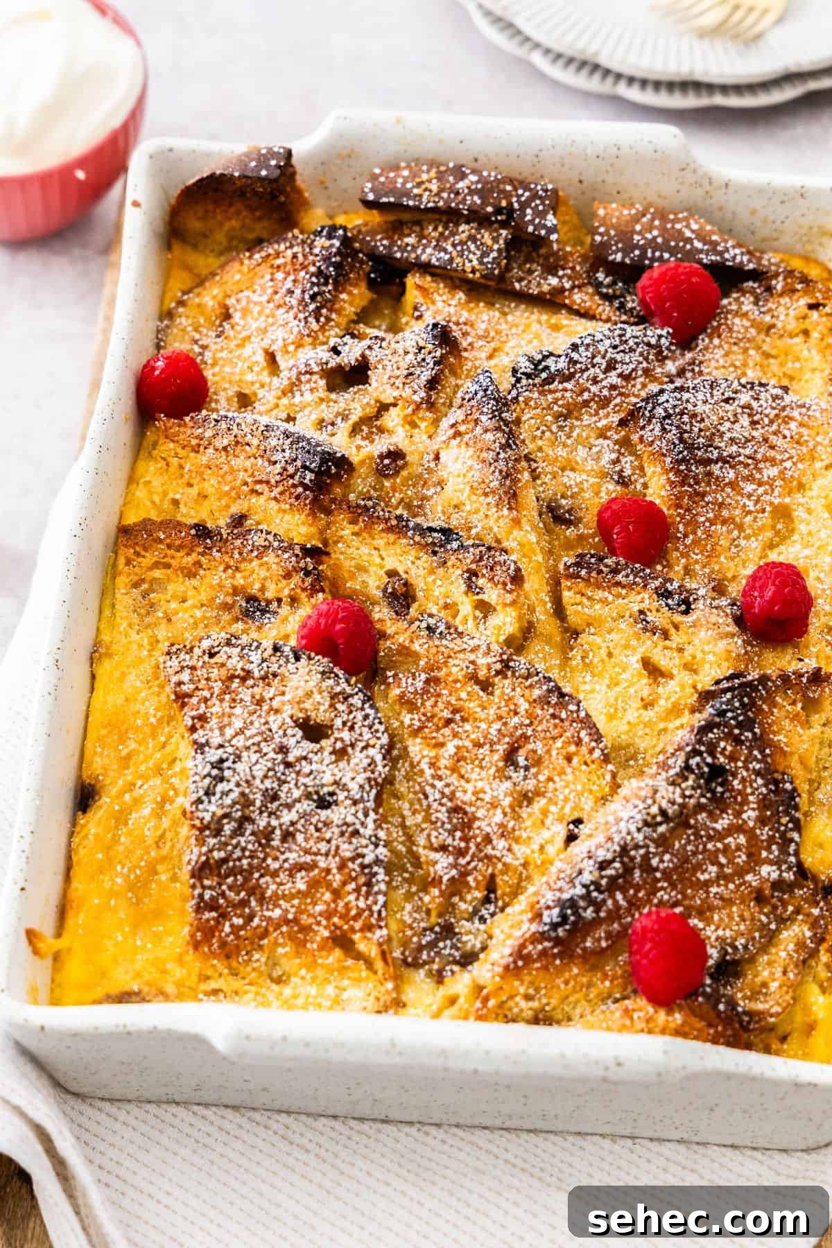 Panettone Bread and Butter Pudding Recipe 2 Large white rectangular dish of Panettone Bread and Butter Pudding, sitting on a white cloth on a wooden board.