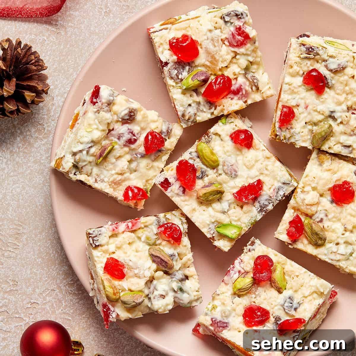 Round pink plate with squares of White Christmas Slice on it, and a couple of Christmas baubles and pine cones around the edge.