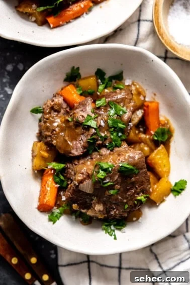 Slow Cooker Corned Beef Recipe for Tender Slices 12 Bowl with pot roast, carrots, and potatoes all garnished with fresh parsley.