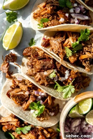 Slow Cooker Corned Beef Recipe for Tender Slices 13 Carnitas Tacos lined up and topped with fresh cilantro, and diced red onion, lime wedges on the side.
