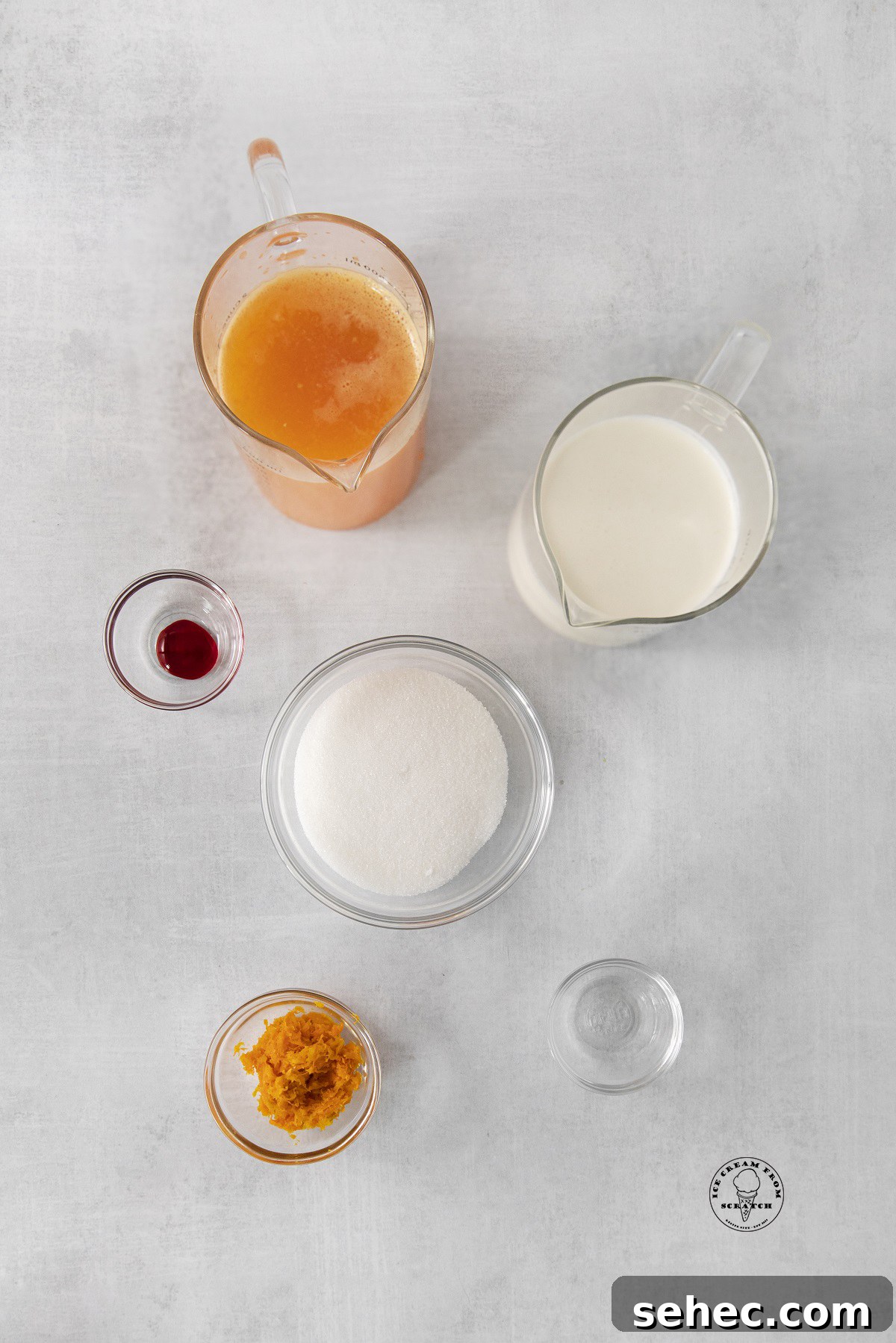 The ingredients needed for making orange sherbet, all in separate bowls and pitchers, arranged on a counter and viewed from above.