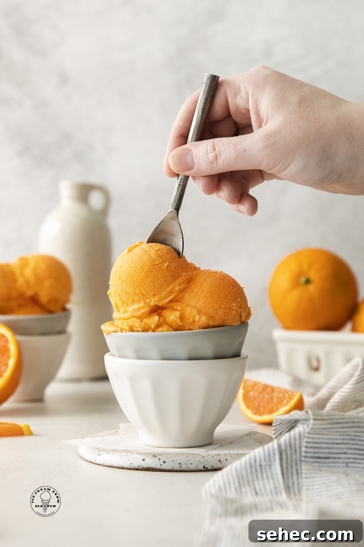 two small bowls stacked, filled with scoops of homemade orange sherbet. A hand is eating it with a small spoon.