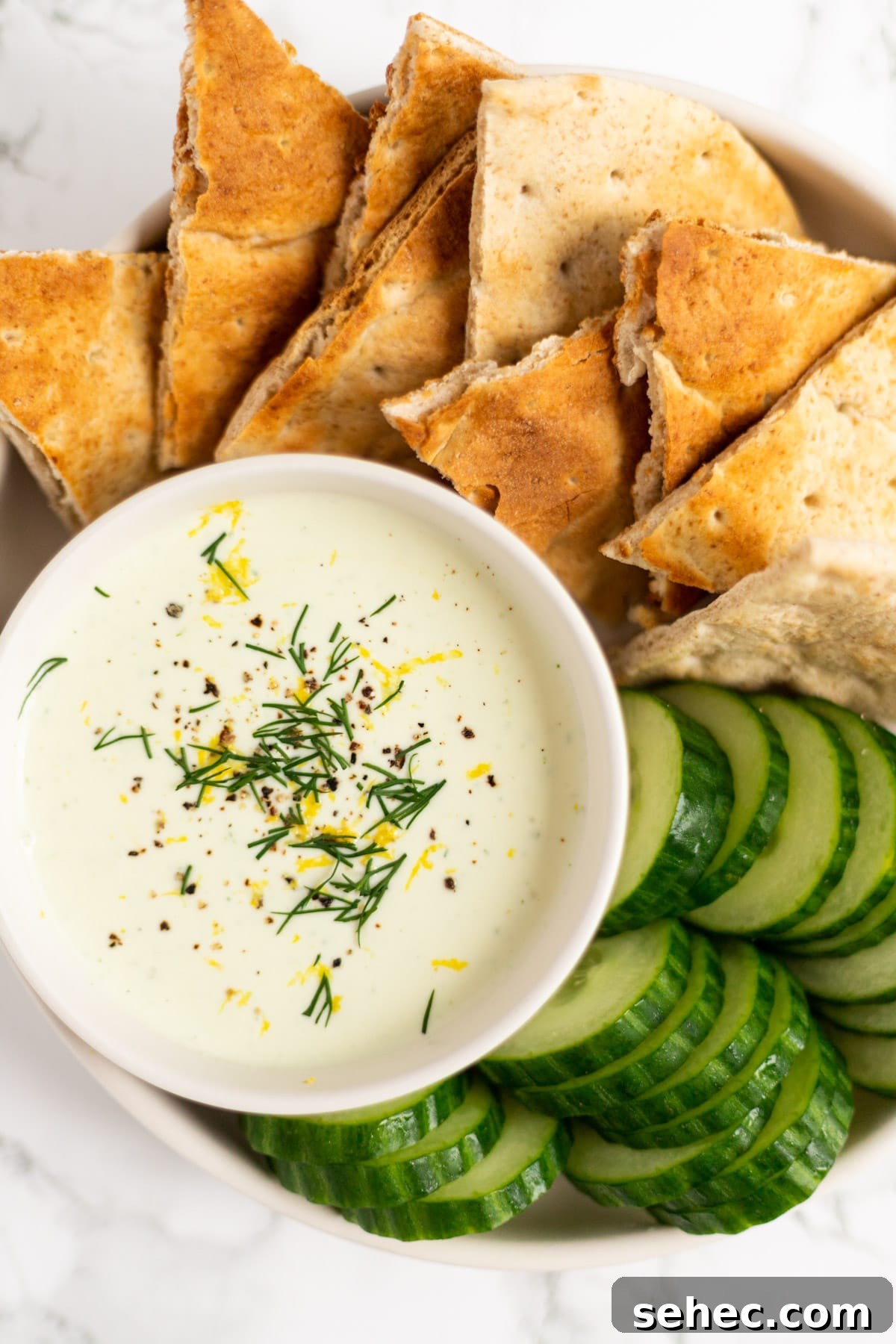 Creamy Whipped Feta Dip with Honey and Herbs 2 A top down view of a bowl of whipped feta dip surrounded by pita and cucumber.