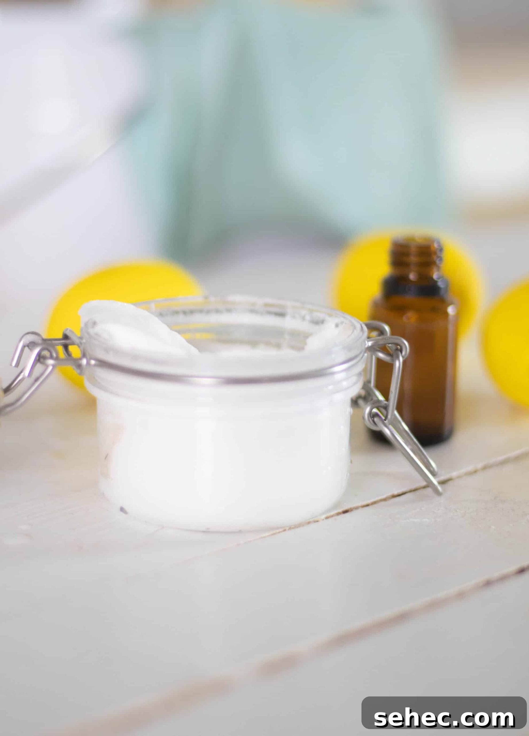 How to Clean Your Home with Natural Products 3 White soft scrub in glass jar on white ship lap with amber essential oil bottle and lemons in background.