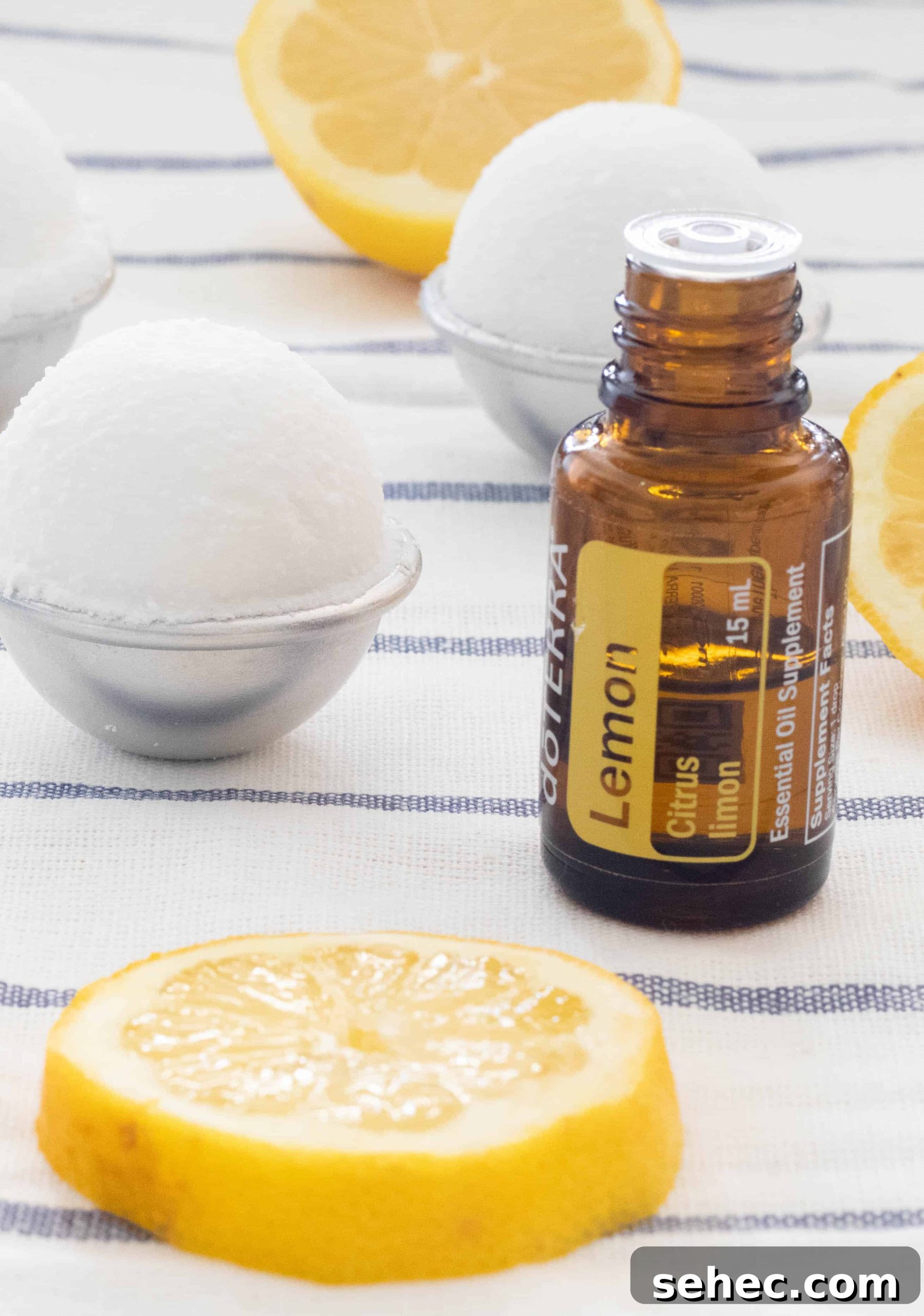 How to Clean Your Home with Natural Products 4 doTERRA lemon essential oil bottle, lemon slices, homemade toilet cleaning bombs on white and blue stripes towel.