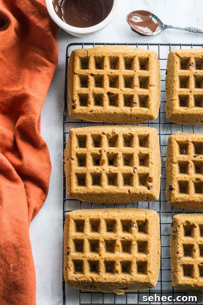 Grain Free Pumpkin Chocolate Chip Waffles 4 Overhead view of grain-free pumpkin chocolate chip waffles cooling on a wire rack beside an orange napkin and melted chocolate.
