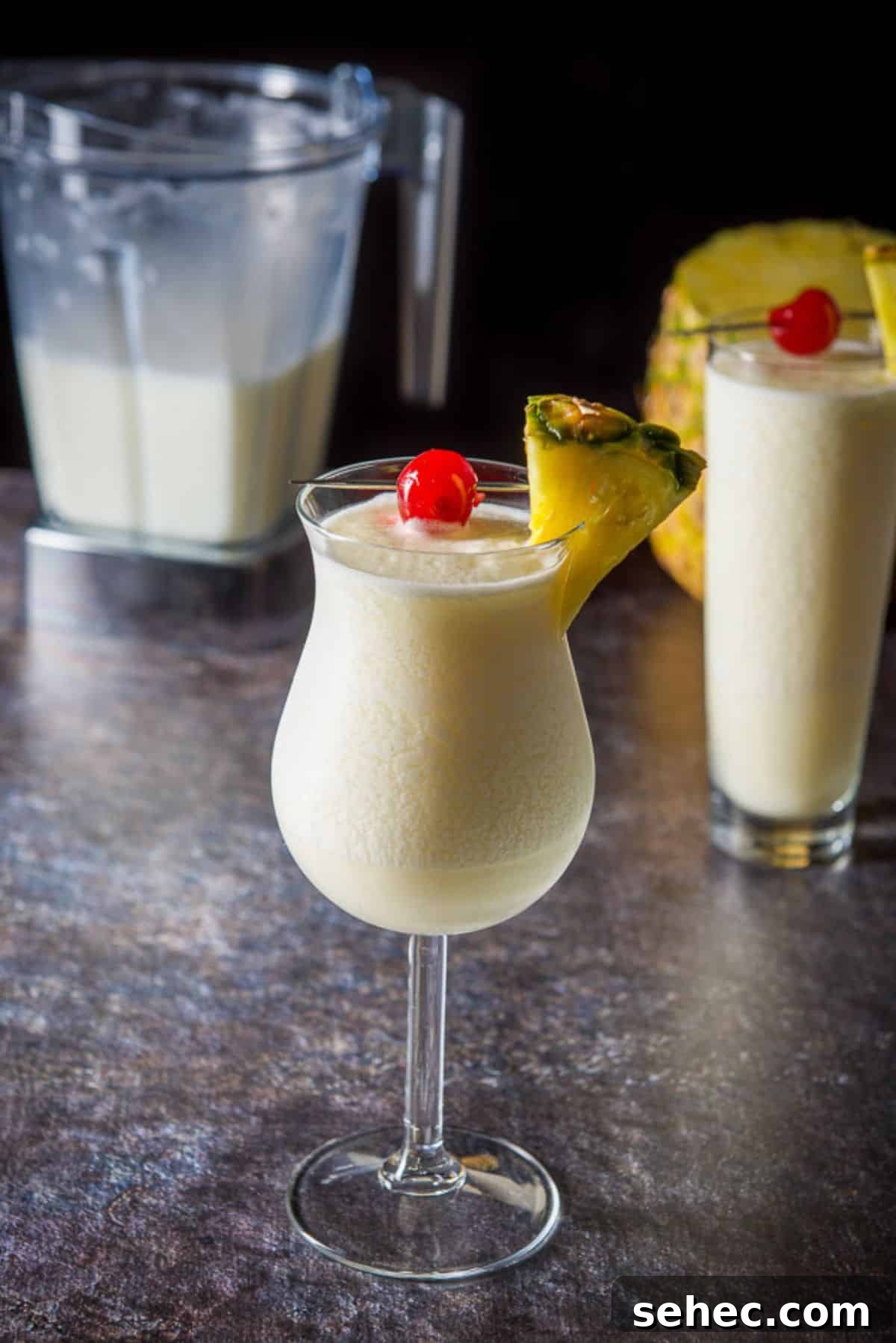 Piña colada cocktail in two glasses with more in the blender behind them